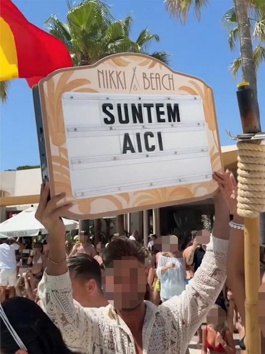 Un bărbat ține o pancartă cu numele resortului pe care scrie „SUNTEM AICI