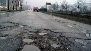 Un pensionar din Santuhalm, de pe DN 7, a semnalizat gropile din fata casei sale cu trunchiuri de brazi!