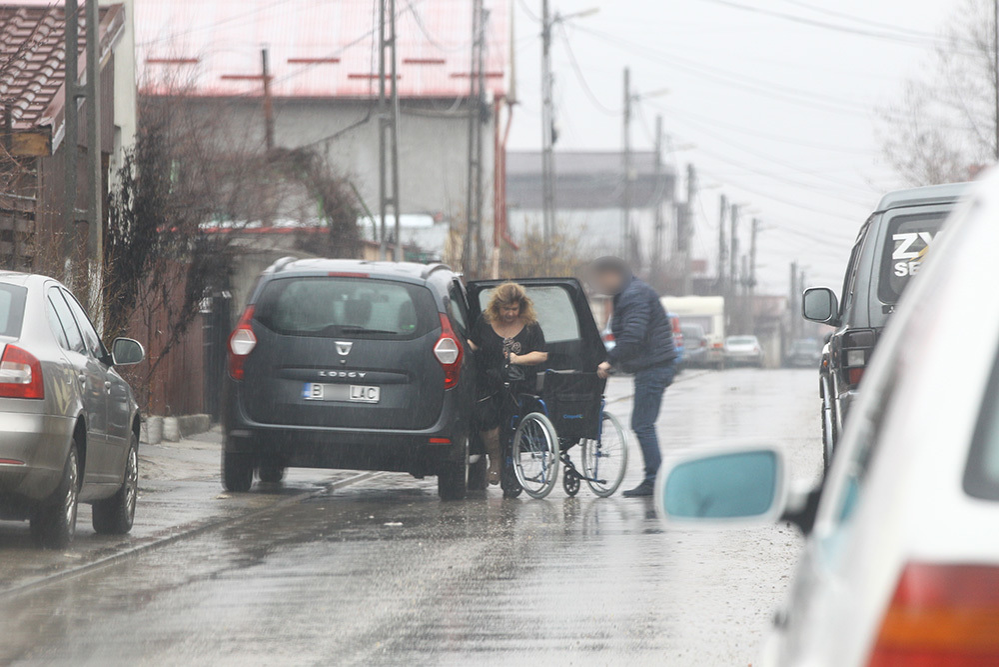 Unul dintre bărbaţi o conduce acasă pe Carmen Orban, ajutând-o cu căruciorul cu rotile