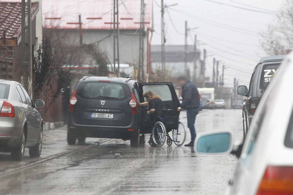Unul dintre bărbaţi o conduce acasă pe Carmen Orban, ajutând-o cu căruciorul cu rotile
