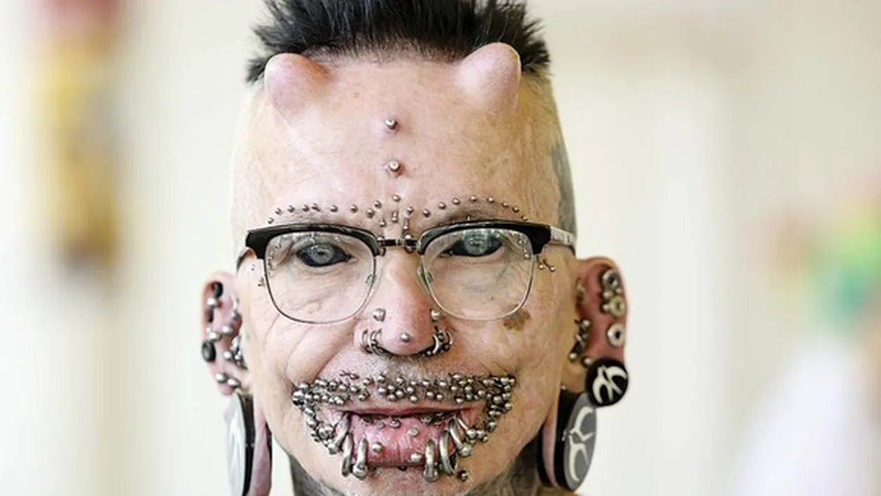 Are 453 de piercinguri, e tatuat tot, are limba despicată și coarne de titan în frunte! Și totul nu se oprește aici