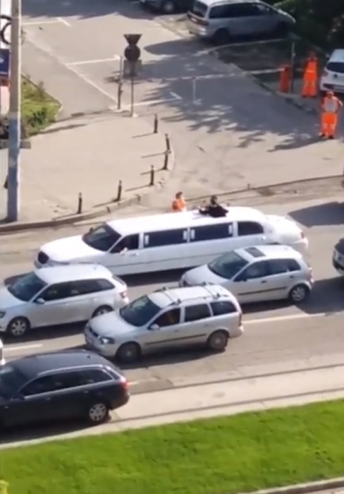 Un muncitor de la asfaltări bea şampanie lângă o limuzină, pe un bulevard din Craiova