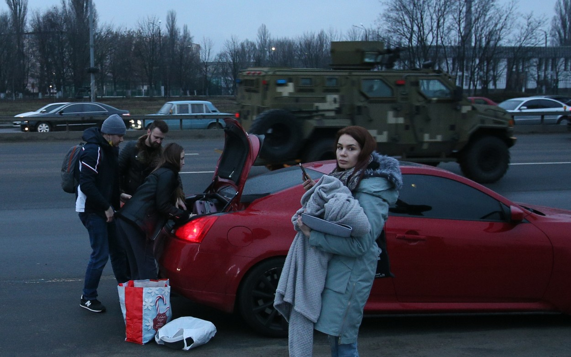 Disperați, oamenii  din Kiev își încarcă lucrurile într-o mașină, în timp ce un vehicul militar trece pe lângă ei. (Sursa foto: profimedia.ro)