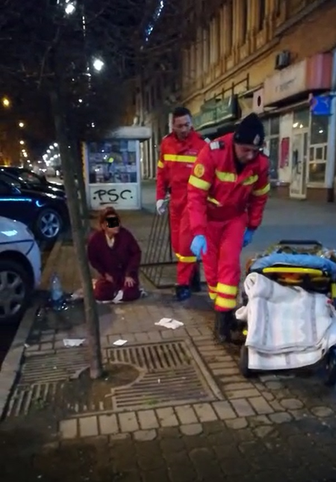 Mama așteaptă în genunchi, pe trotuar, să fie urcată în ambulanță